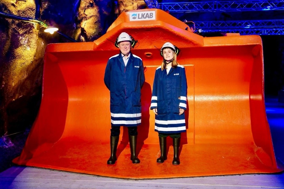 Ambassador Bengt van Loosdrecht and Second Secretary Jara Verkleij pose in front of a large LKAB digging machine in Kiruna