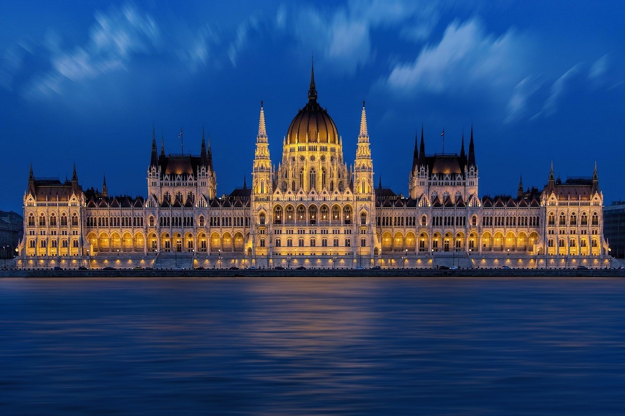 A view of the Parliament of Hungary across the River Danube, lit against the backdrop of the evening sky