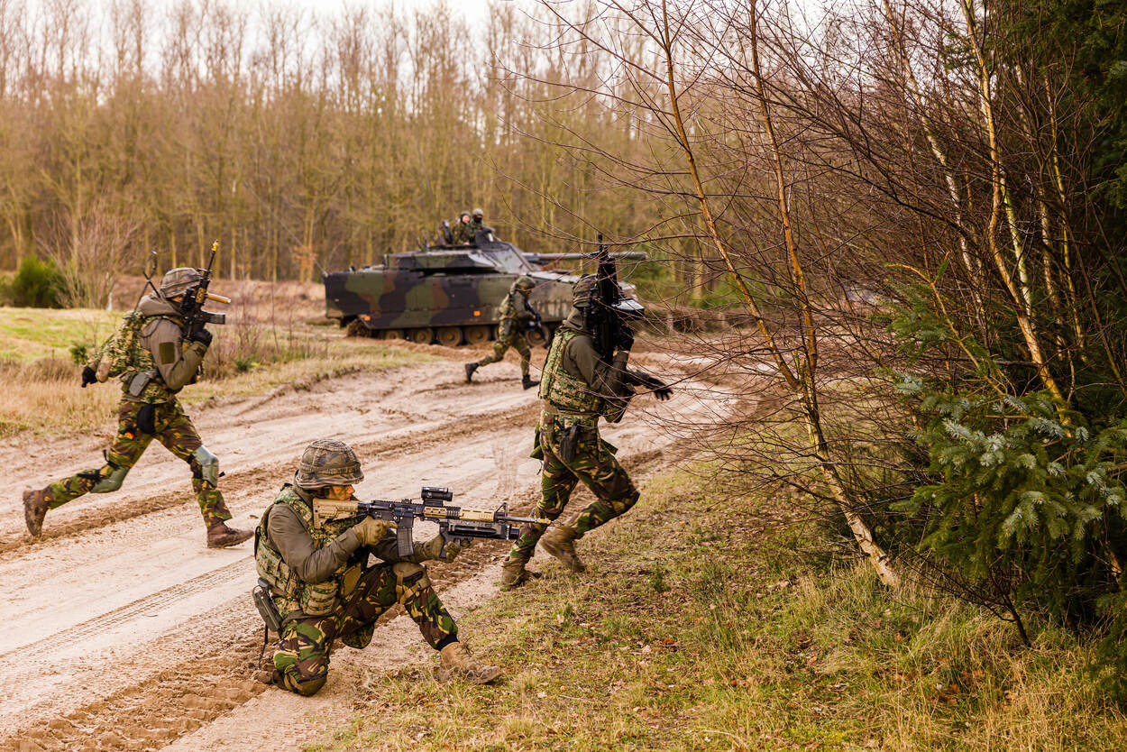 people in military clothes in action with a tank in the background